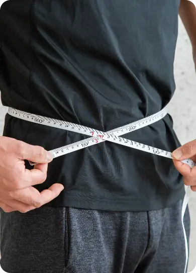 Person measuring their waist with a tape to track weight loss progress.