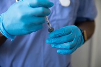 Healthcare professional wearing blue gloves drawing peptide solution from a vial with a syringe